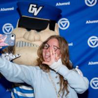 Grad gives anchor up sign with Louie in front of Alumni backdrop